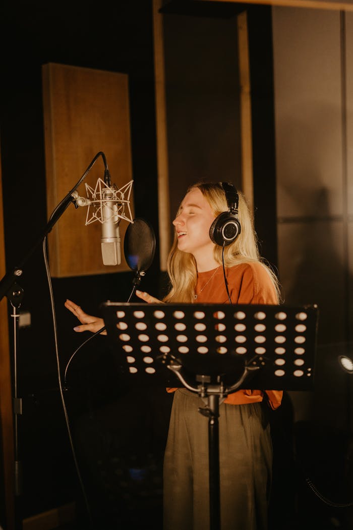 Young woman singing passionately in a recording studio with headphones and mic.